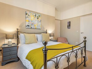 A neatly arranged bedroom with a bed, bedside tables, a chair, and a painting on the wall. - Bank House Apartment (Newnham, Forest of Dean,)