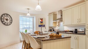 Een moderne keuken met een centraal eiland, barstoelen, een klok en een raam.