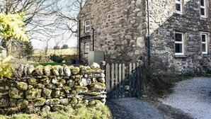 A stone house with a sloped roof, a stone wall in front, and a gravel driveway.