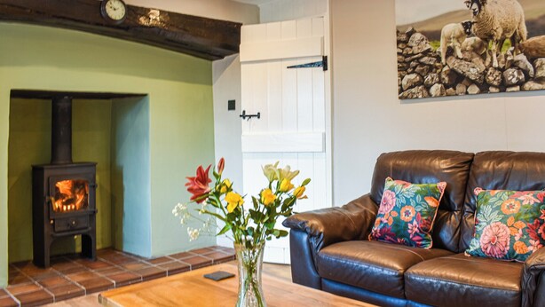 A living room with a fireplace, a sofa with floral cushions, and a vase of flowers on a coffee table.