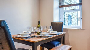 A dining table set with wine glasses, plates, and a bottle, with chairs around it.