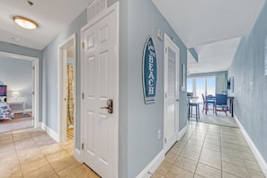 A hallway with a door leading to a bedroom, a dining area with chairs, and a wall sign that says "Gone to the Beach." - Ocean View- Laketown Wharf 1809 (Panama City Beach)