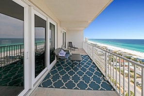A balcony with a patterned floor, two chairs, a small table, and a view of the beach.