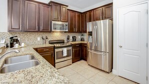 A kitchen with dark wooden cabinets, stainless steel appliances, a tiled backsplash, and a double sink.