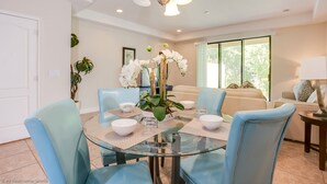 A dining area with a glass table, blue chairs, white bowls, and a vase of white orchids.