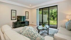 A modern living room with a sofa, a coffee table, a TV, and a sliding glass door leading to a garden.