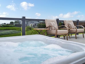 A hot tub with two lounge chairs and a table on an outdoor deck.