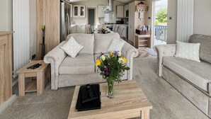 A modern living room with a sofa, a coffee table, and a kitchen in the background. - Reel Paradise - UK37723 (Addlethorpe, near Skegness)