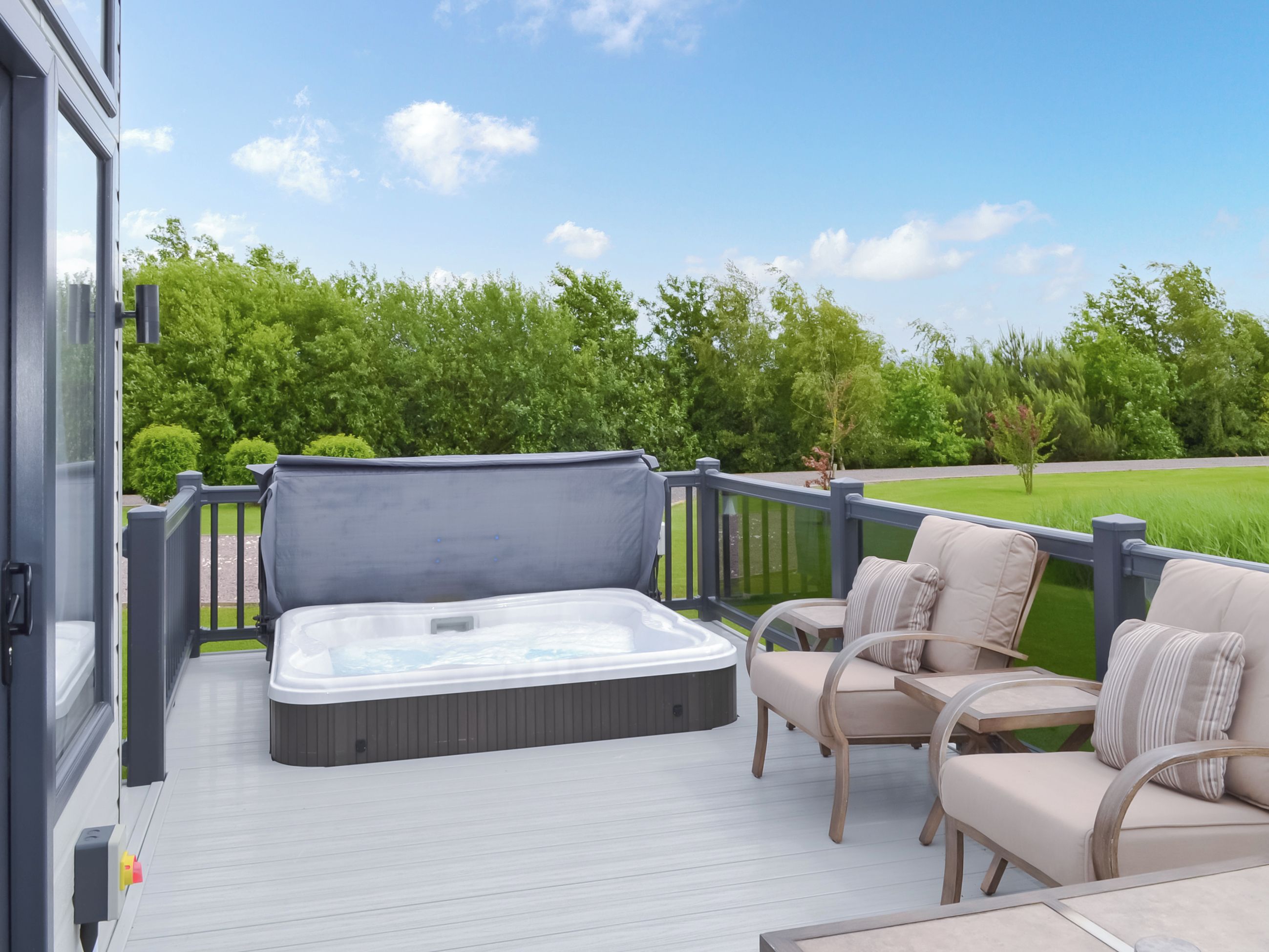A hot tub on a deck with chairs and a view of a green landscape.