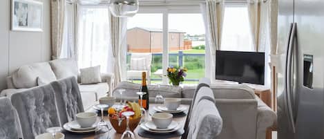 Una sala de estar moderna con comedor, un ventanal con cortinas, un televisor de pantalla plana y un refrigerador.
