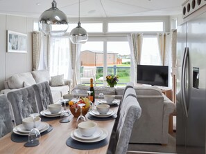 A modern living room with a dining area, a large window with curtains, a flat-screen TV, and a refrigerator.