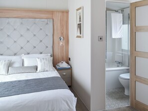 Ein Schlafzimmer mit einem gepolsterten Kopfteil, einem Nachttisch mit Lampe sowie ein Badezimmer mit Dusche und Toilette.