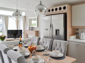 Eine moderne Küche mit einem Einbaukühlschrank, einem Esstisch gedeckt mit Tellern, Schüsseln und Gläsern, sowie einem Fernseher auf einem Standfuß.