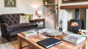 A living room with a sofa, coffee table, books, a lamp, a mirror, and a wood-burning stove. - 2 bedroom accommodation in Gargrave, near Skipton (Skipton)
