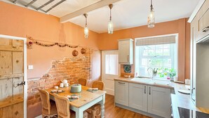 A kitchen with a brick wall, wooden dining table, chairs, and hanging light fixtures. - 2 bedroom accommodation in Gargrave, near Skipton (Skipton)