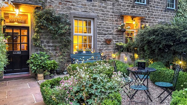 A stone building with a black door labeled 'HONEY COTTAGE,' a bench, and outdoor seating with tables and chairs. - 2 bedroom accommodation in Gargrave, near Skipton (Skipton)