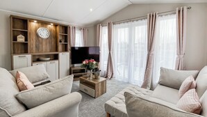 Ein Wohnzimmer mit Sofa, Hocker, einer Holz-Unterhaltungsecke, Fernseher und Vorhängen.