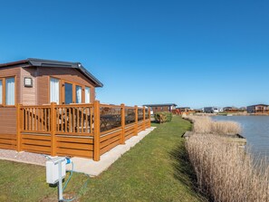 Une rangée de cabanes en bois, avec une zone herbeuse et une étendue d’eau.
