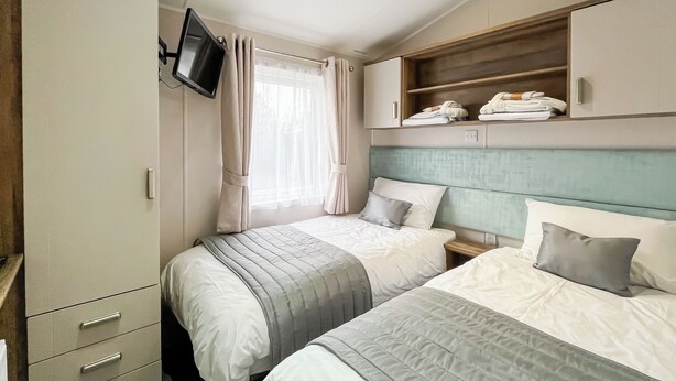 Ein Schlafzimmer mit zwei Betten, einem an der Wand befestigten Fernseher und einem Schrank mit Schubladen.