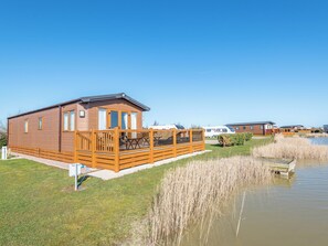 A wooden cabin with a deck, a grassy area, and a body of water.