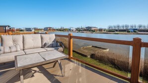 Eine Terrasse mit einer Couch und einem Tisch, mit Blick auf ein Gewässer und Häuser im Hintergrund.