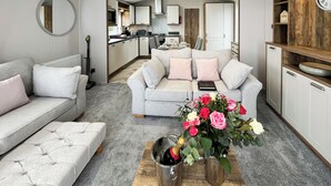 Ein modernes Wohnzimmer mit einem grauen Sofa, einem Couchtisch mit einer Champagnerflasche und einer Küche im Hintergrund.