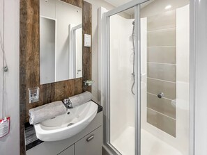 Une salle de bain moderne avec un lavabo blanc, un miroir, une serviette et une cabine de douche en verre.