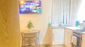 A compact kitchen with a dining area, a flat-screen TV mounted on the wall, and a small round table with chairs. - Citywide Hospitality (Liverpool)