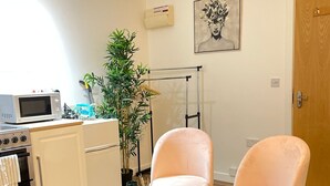 A modern kitchen with white cabinets, a microwave, and a stove. There is a blue rug, two pink chairs, and a potted plant. - Citywide Hospitality (Liverpool)