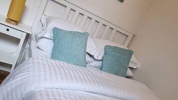 A neatly made bed with white and striped bedding, a white headboard, and two teal pillows.