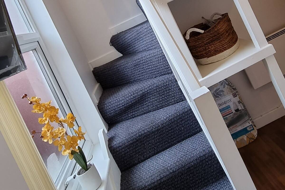 A staircase with a white railing, a dark carpeted floor, and a basket on a shelf.