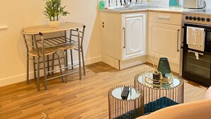 A compact kitchen with a dining area, a TV mounted on the wall displaying various shows, a small potted plant, and a modern coffee table. - Citywide Hospitality (Liverpool)