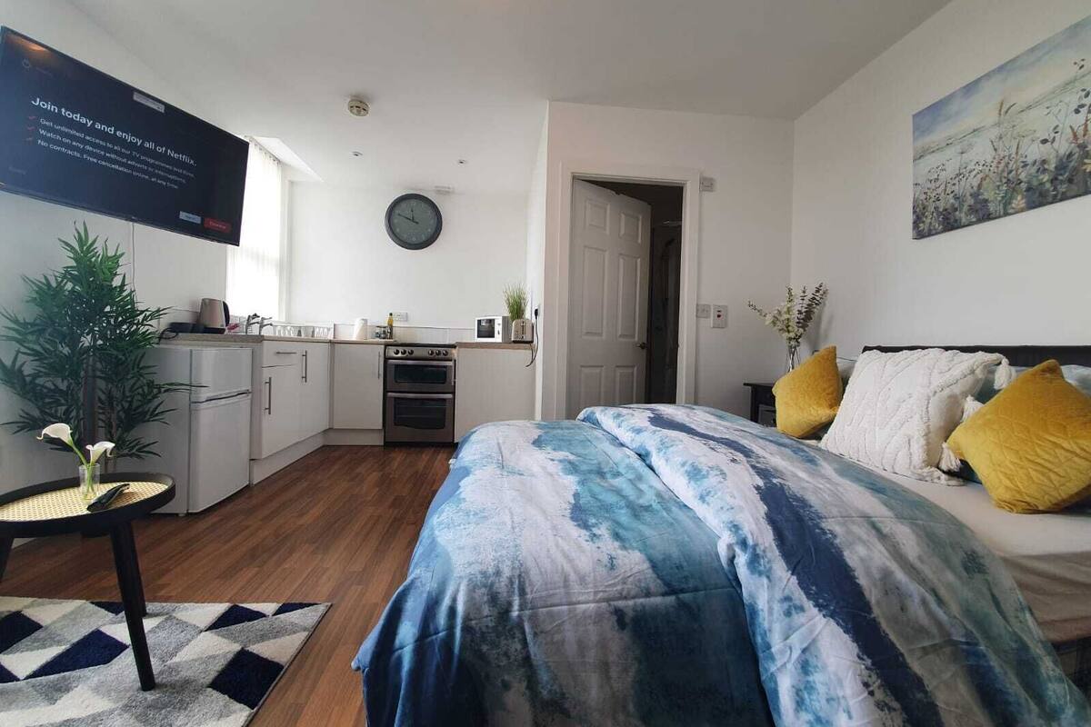 A modern bedroom with a large bed, a small kitchenette, and a view of the outdoors.