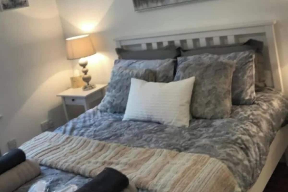 A neatly made bed with a patterned bedspread, a bedside lamp, and a framed picture on the wall.