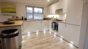 A modern kitchen with white cabinets, a wooden countertop, and a stainless steel trash bin. - Hollicarrs - The Rushes (York)