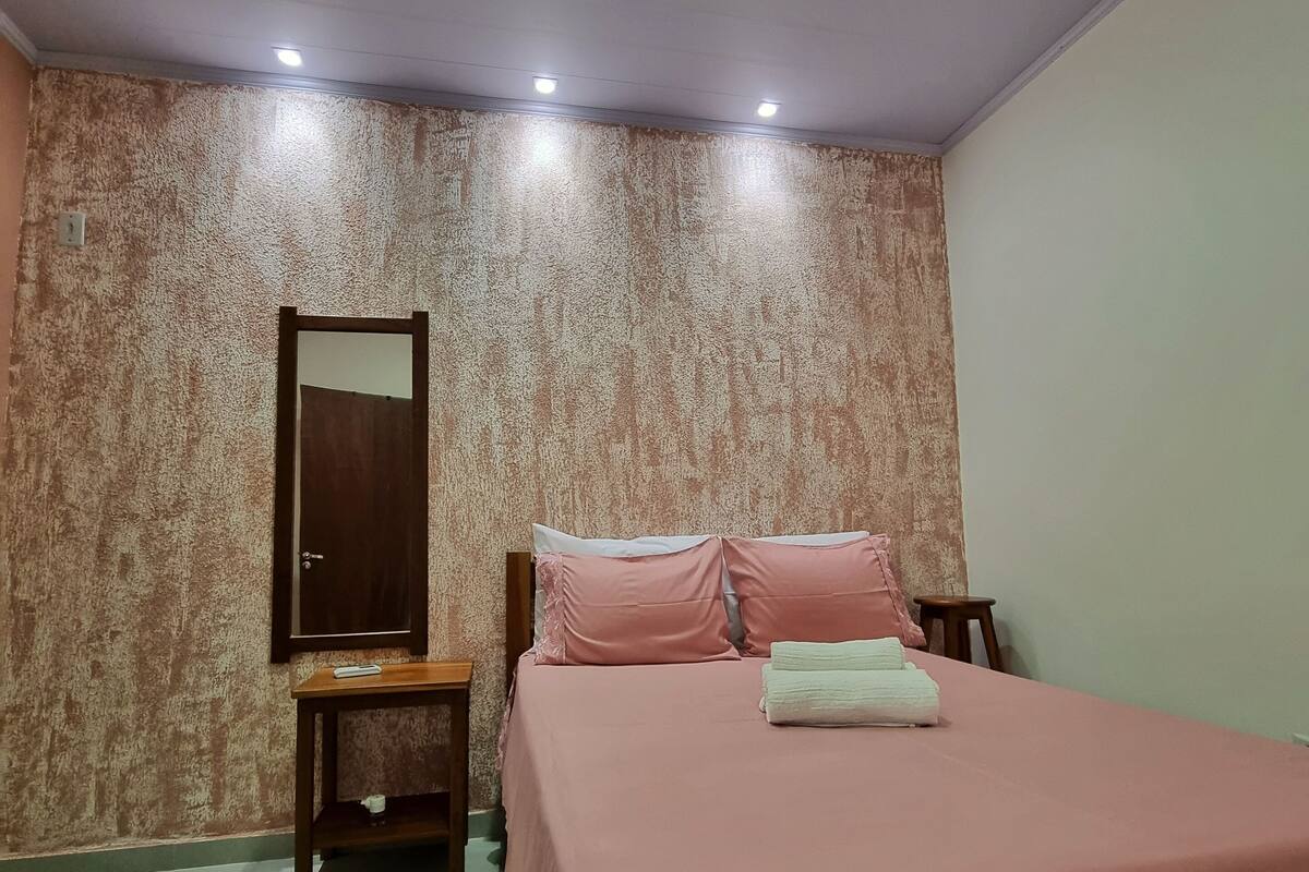 A bedroom with a bed, a nightstand, a mirror, and a wall with a textured pattern.