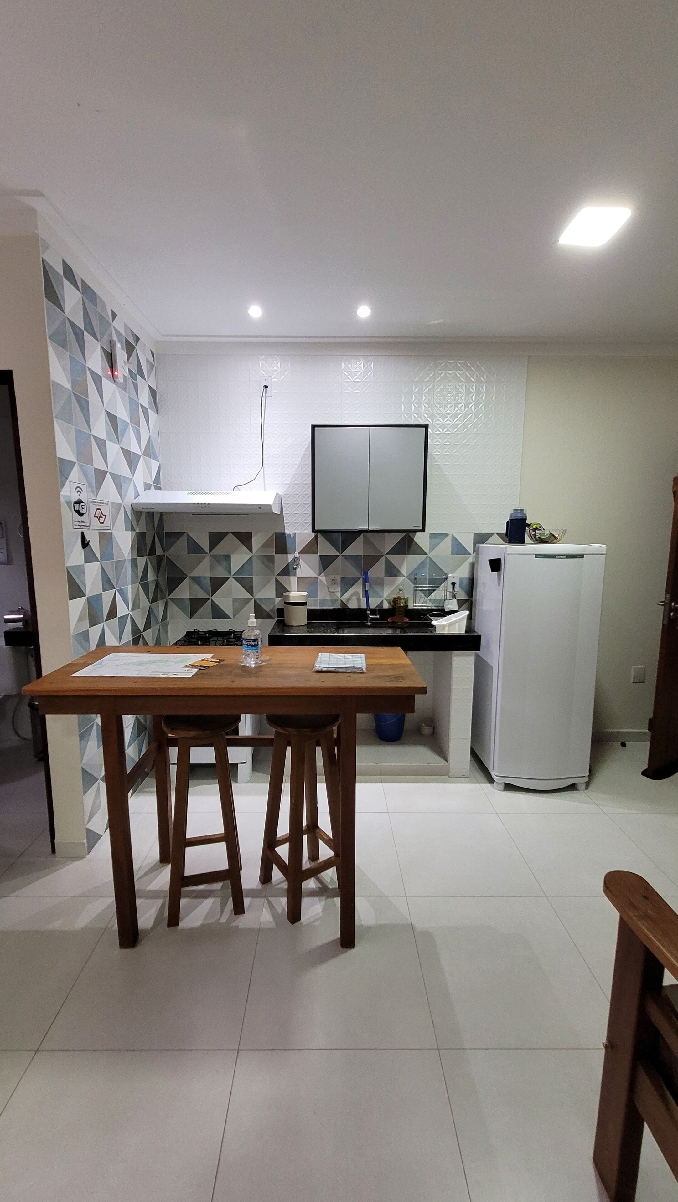 A compact kitchen with a dining table, stools, a refrigerator, and a microwave.