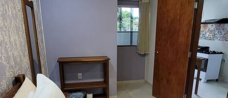 Un dormitorio con cama, cabecero de madera, mesita de noche con lámpara, armario y ventana con vistas al exterior.