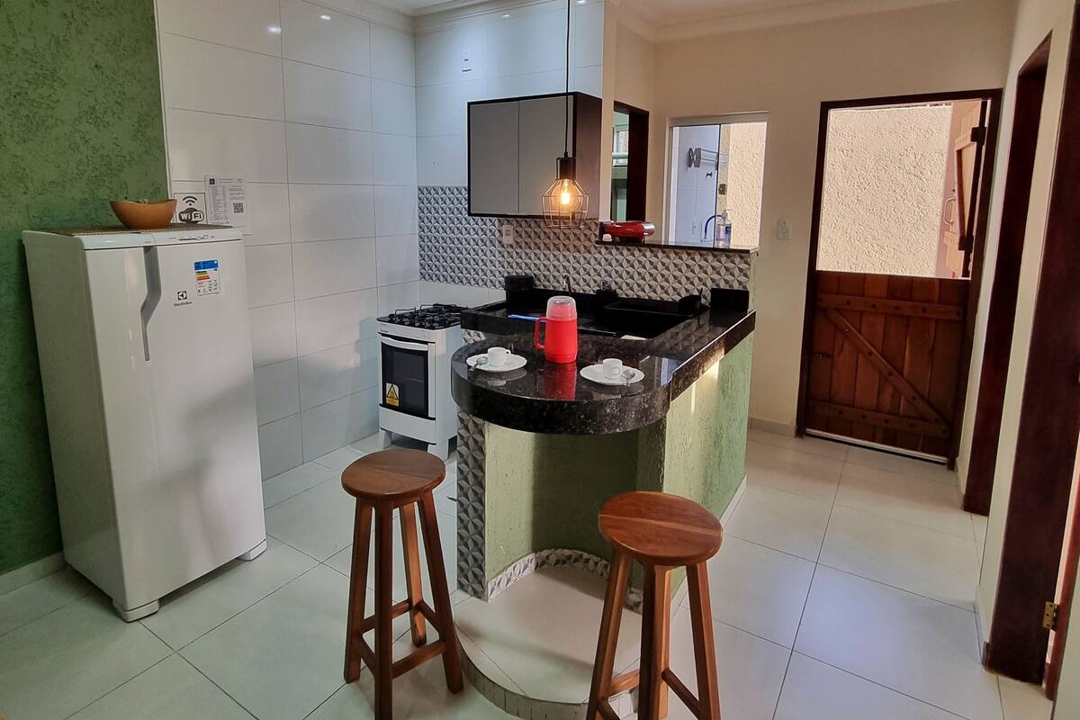 A modern kitchen with a central island, two wooden stools, a refrigerator, and a stove.