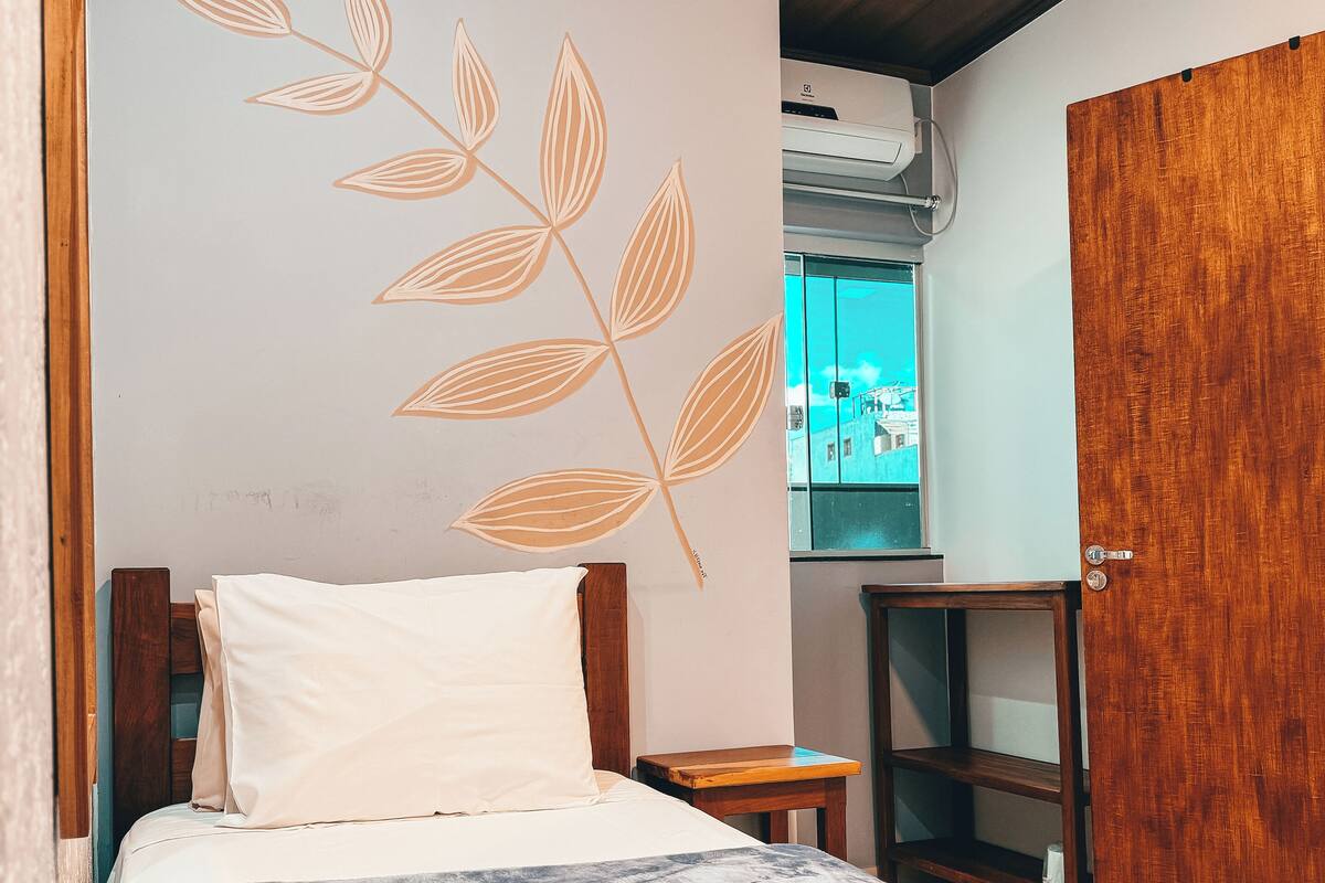 A bedroom with a bed, a wooden headboard, a wall with a leaf pattern, a wooden wardrobe, and a small wooden nightstand.