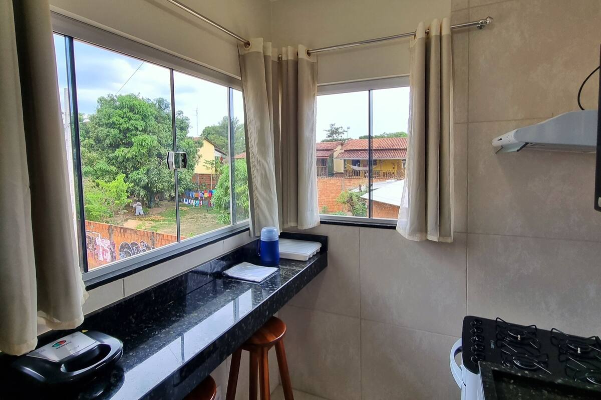 A kitchen with a long counter, two stools, a stove, and a window with curtains.