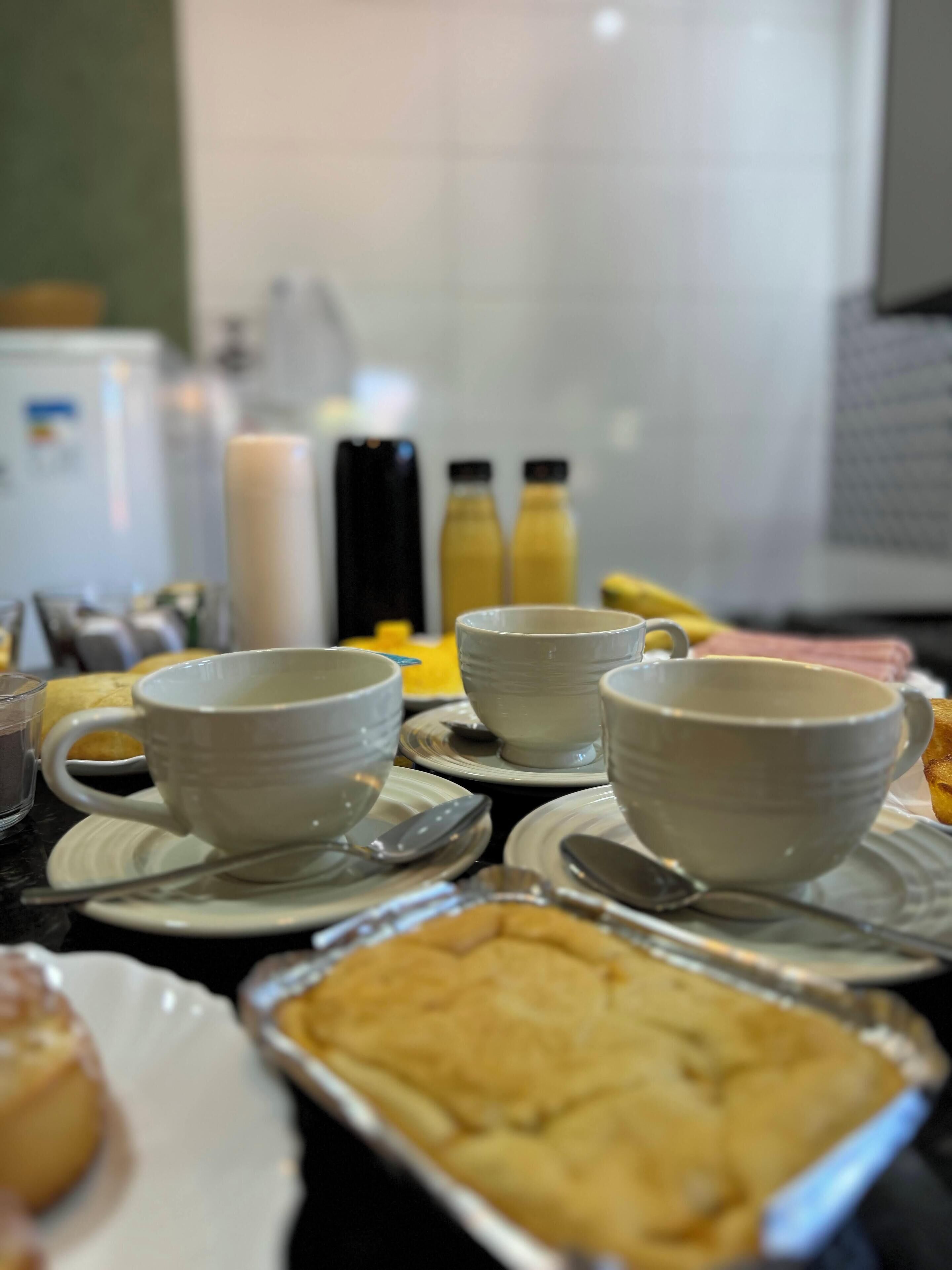 A breakfast setting with white cups, spoons, and a tray of food.