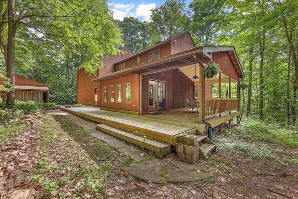 Een houten chalet met terras en overdekte veranda, omgeven door een bos.