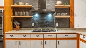 A kitchen with a stone backsplash, wooden shelves, and a built-in stove.