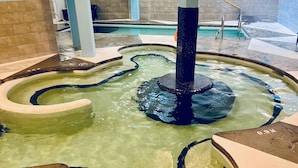 Uma banheira de hidromassagem com design circular e uma coluna central, rodeada por um espaço revestido com azulejos.