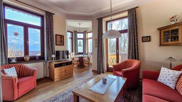 A spacious living room with a wooden coffee table, red sofas, a TV, and a dining area with chairs and a table.