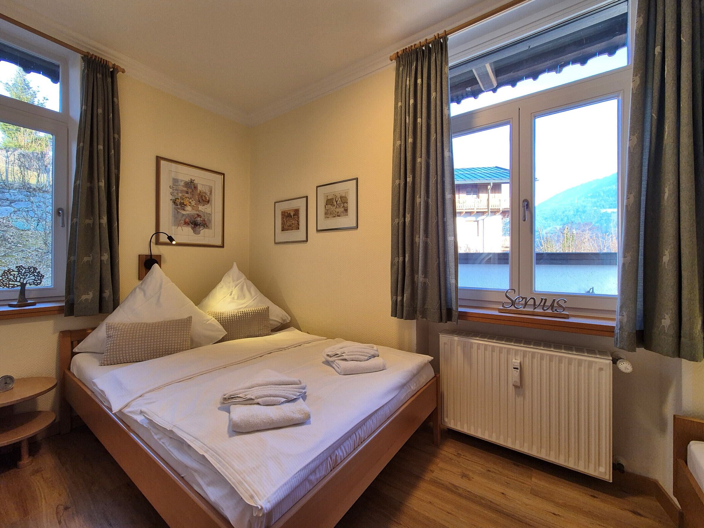 A bedroom with a bed, two bedside tables, a window with curtains, and framed pictures on the wall.