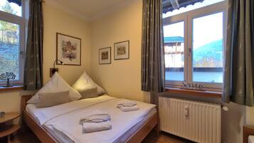 A bedroom with a bed, two bedside tables, a window with curtains, and framed pictures on the wall.