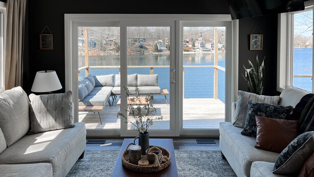 Una sala de estar moderna con un amplio ventanal corredera que da a una terraza con vistas a un cuerpo de agua.