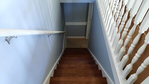 Un escalier en bois avec des balustrades blanches, menant à un palier doté d’une main courante blanche.